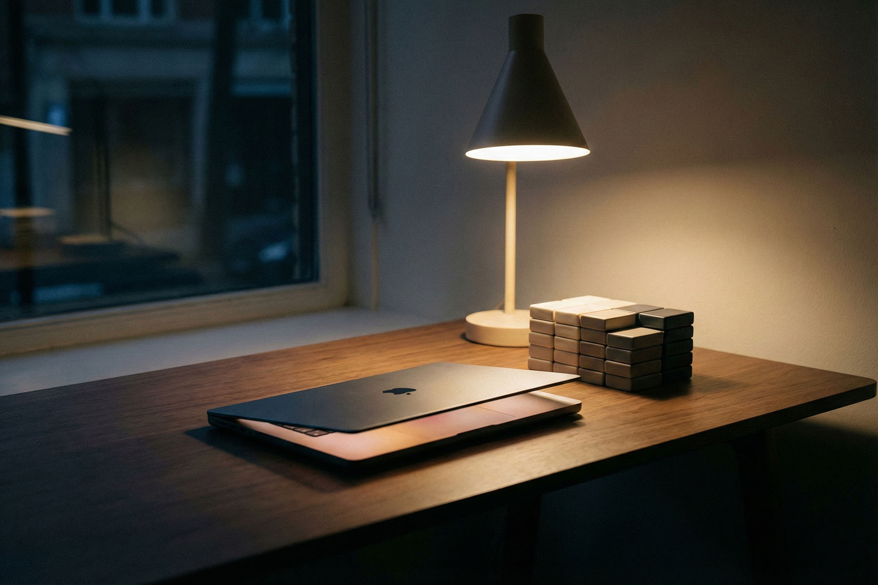 Laptop under a desk lamp beside stacked blocks, suggesting SEO systems, diagnostics, and content infrastructure workflow.
