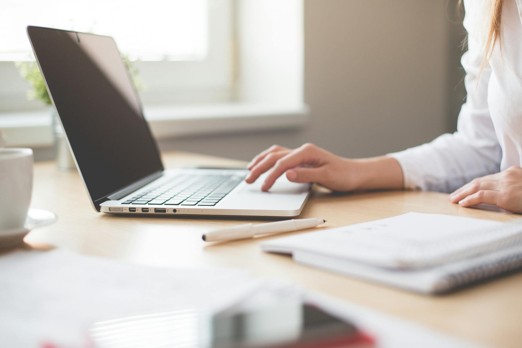 Person typing on laptop at clean desk with notebook and pen nearby for content planning. Image by picjumbo.com (https://www.pexels.com/@picjumbo-com-55570)